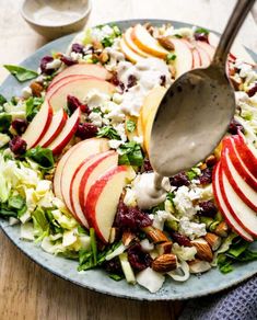 a salad with apples, cranberries and nuts is being drizzled with dressing