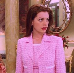 a woman in a pink suit standing next to a mirror