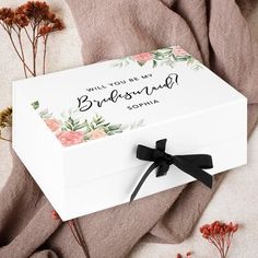 a white box with black ribbon and flowers on the side that says, will you be my bridesma?