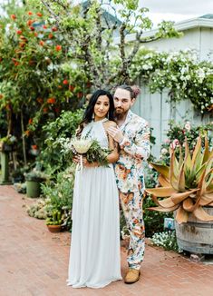 a man and woman standing next to each other in front of some potted plants