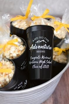 some black cups filled with popcorn and yellow ribbon tied around the top one cup is labeled and so the adventure begins