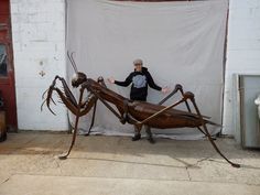 a man standing next to a large metal insect statue in front of a white wall