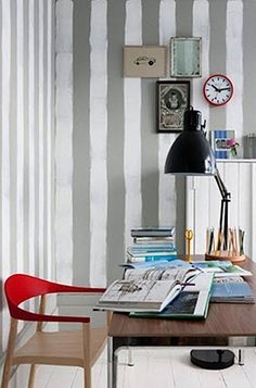 a desk with a lamp, books and pictures on the wall next to a clock