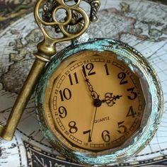 an antique pocket watch sitting on top of a map with a key attached to it