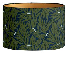 a green lamp shade with white birds flying over the leaves and branches on blue background