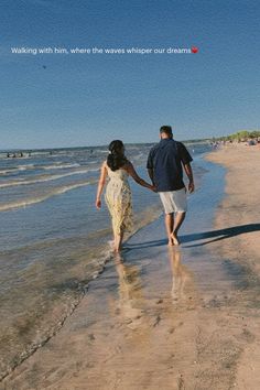 a man and woman walking on the beach holding hands with an ocean in the background