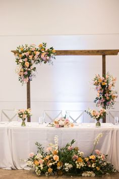 an arrangement of flowers and greenery on a white table cloth draped over the tables