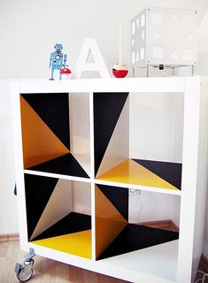 a toy robot is sitting on top of a bookcase that has geometric shapes painted on it