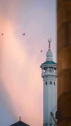 a tall white tower with a clock on it's side and birds flying around