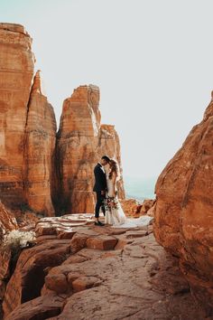 a bride and groom standing in front of rock formations at their wedding venue, surrounded by red rocks