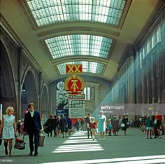 many people are walking around in an old train station with high ceilings and large windows