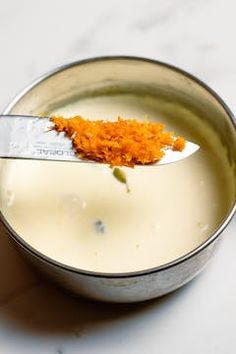 a spoon with some food in it on top of a bowl filled with milk and orange zest