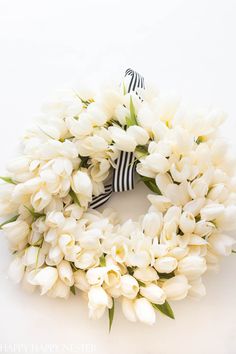 a wreath with white tulips and a black bow on it is sitting against a white background