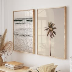 two framed pictures hang on the wall above a table with books and plants in vases