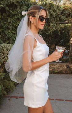 a woman in a white dress holding a wine glass and wearing a veil on her head