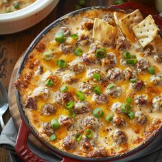 a casserole dish with cheese, meatballs and green onions in it on a wooden table