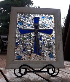 a blue and white cross made out of glass on top of a wooden table next to a tree