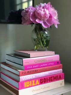 a stack of books sitting on top of a table next to a vase filled with flowers