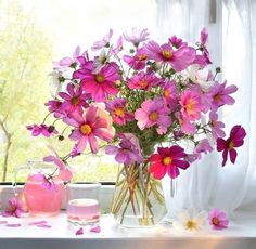 a vase filled with pink flowers sitting on top of a table next to a window