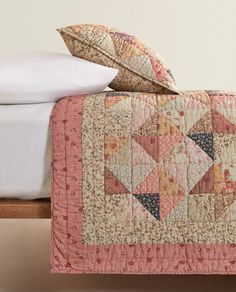 a bed with a quilt and pillows on top of it next to a white pillow