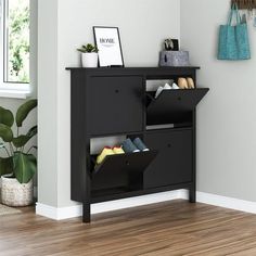 a black shelf with shoes on it in front of a white wall and wooden floor