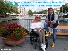 a man sitting next to a woman in a wheel chair on a bridge near flowers