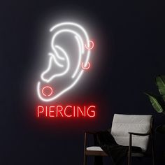 a neon sign that says piercing in front of a black wall with a chair and potted plant