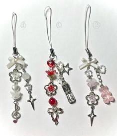 three pairs of earrings with charms attached to them on a white surface, one is red and the other is silver