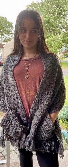 a woman standing in front of a fence wearing a sweater with fringes on it