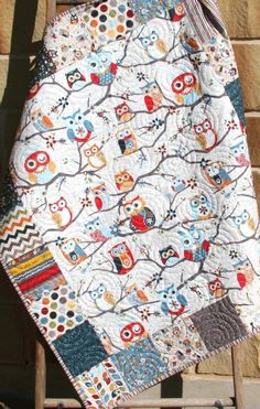 an owl themed baby quilt hanging on a chair next to a brick wall and wooden ladder