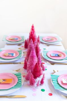 the table is set with pink and green plates, silverware, and feather trees