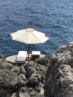 two chairs and an umbrella on the rocks by the water