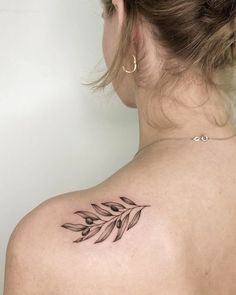 the back of a woman's shoulder with a leaf tattoo on her left arm