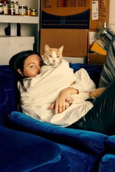 a woman laying on top of a blue couch next to a cat