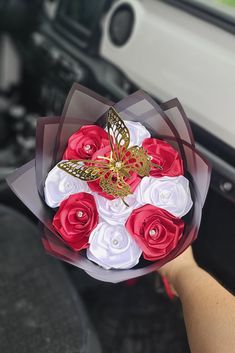 a person holding a bouquet of red and white roses in their hand with a gold butterfly on it