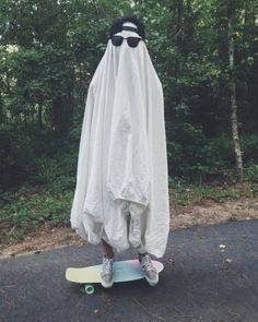 a person in a white cloak and sunglasses on a skateboard with trees in the background