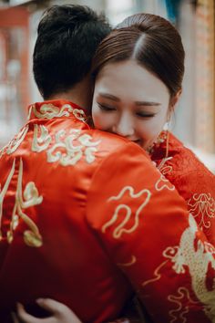 a man and woman embracing each other in traditional chinese dress, both wearing red jackets