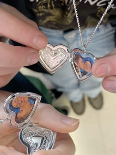 two people are holding some silver heart shaped pendants with pictures on them and one is wearing a necklace