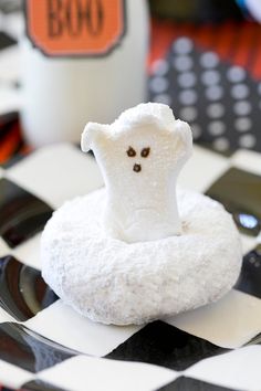 a small marshmallow ghost sitting on top of a black and white checkered table cloth