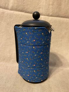 a blue flowered pot with a black lid sitting on top of a white cloth