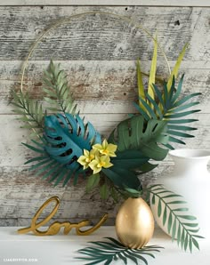 a gold vase with green leaves and flowers next to a love sign on a shelf