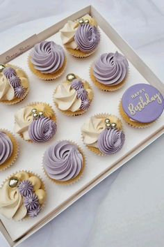 twelve cupcakes with purple frosting in a box on a white tablecloth