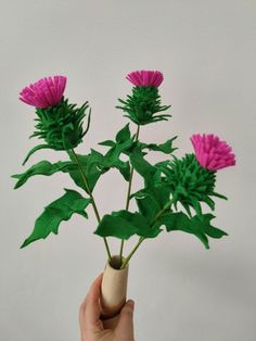 a hand holding a fake pink flower with green leaves