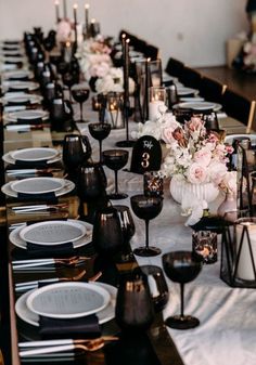 a long table is set with black and white plates, silverware, and flowers