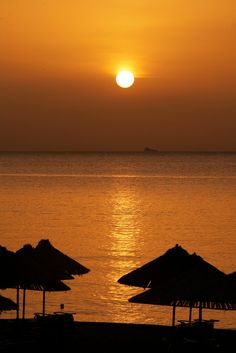 the sun is setting over the ocean with straw umbrellas