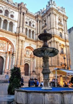 a fountain in front of an old building with people sitting around and eating at it