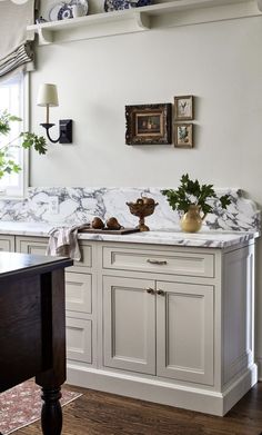 a kitchen with white cabinets and marble counter tops, along with potted plants on the wall