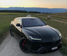 a black sports car parked on the side of a dirt road next to a field