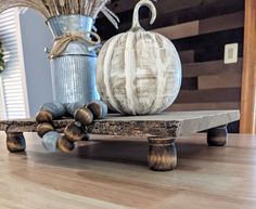 two pumpkins sitting on top of a wooden table next to a vase with dry grass in it