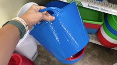 a person is holding a blue bucket in front of some plastic cups and bowls on the shelf